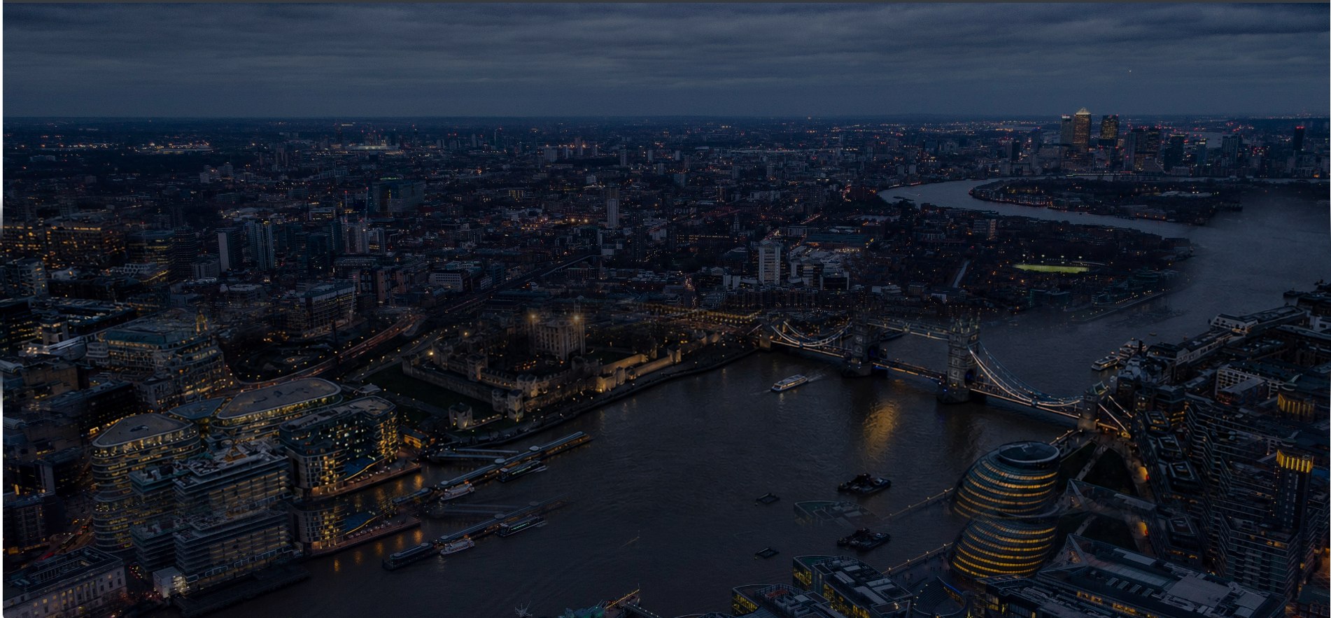 Aerial view of the River Thames at night, with Tower Bridge, the Tower of London and the lights of Canary Wharf in the distance